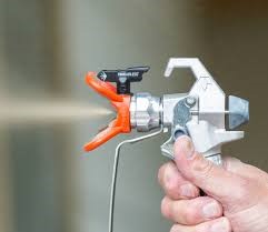 a spray gun shooting out a liquid with a hand pressing down on the trigger